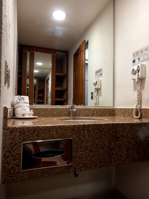 Un baño con encimera de granito, un lavamanos, un espejo y un perchero para toallas.