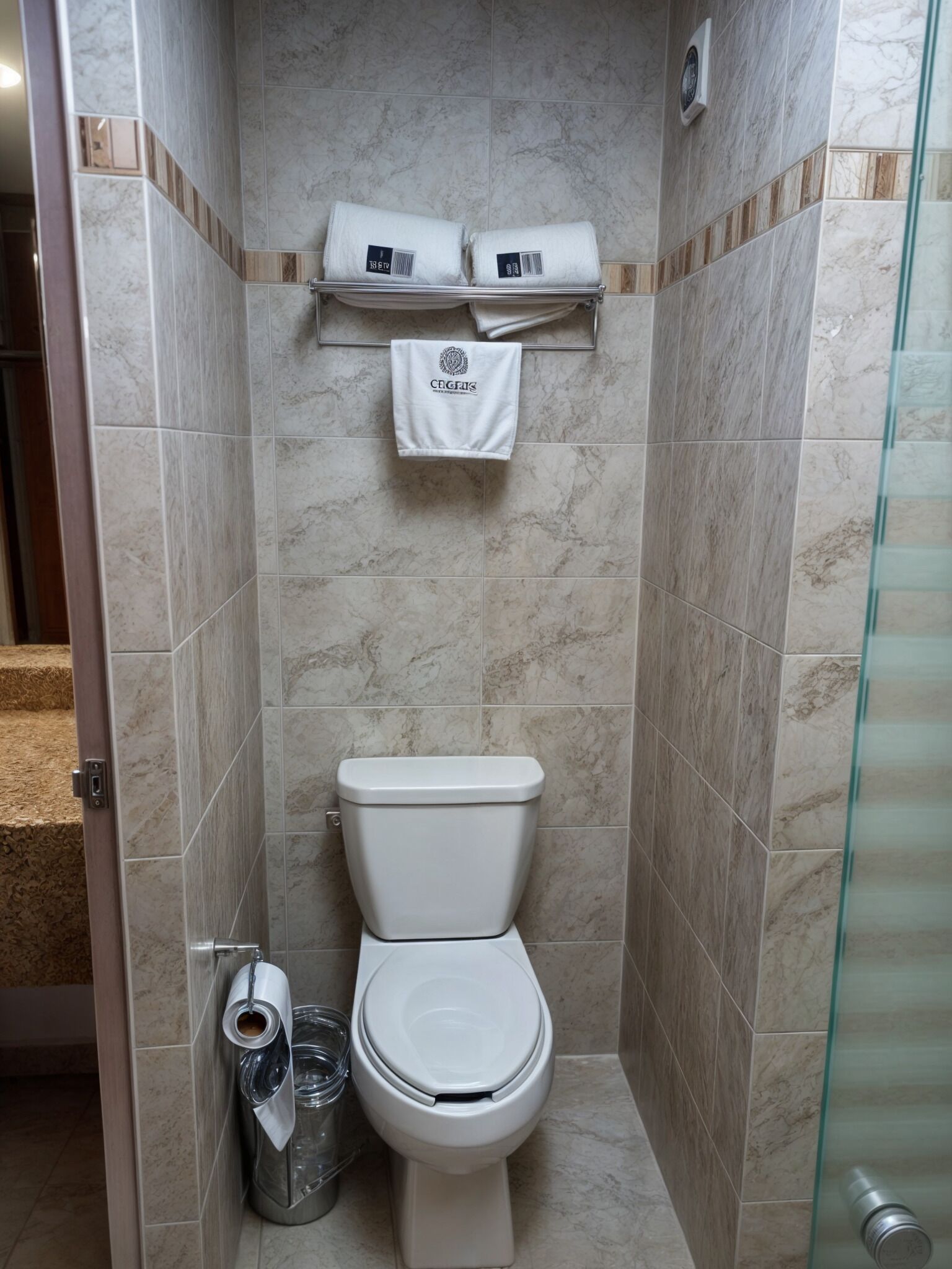 Un baño con inodoro, cabina de ducha de vidrio y un toallero con dos toallas.
