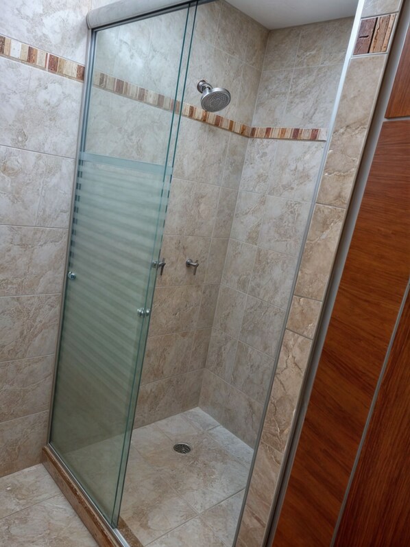 A glass-enclosed shower stall with a marble-tiled wall, a wooden door frame, and a showerhead. - Hotel Soleil Business Class Celaya (Celaya)