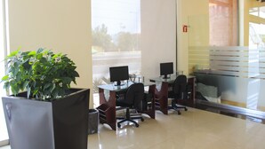 Un espace de bureau moderne avec des cloisons en verre, plusieurs postes de travail informatiques et une plante en pot.