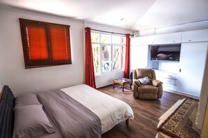 Une chambre à coucher avec un lit, une chaise, un téléviseur et une fenêtre avec des stores.