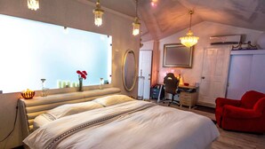 A bedroom with a large bed, a desk, a chair, a mirror, and a chandelier. - Angel's Cave (Escazu)
