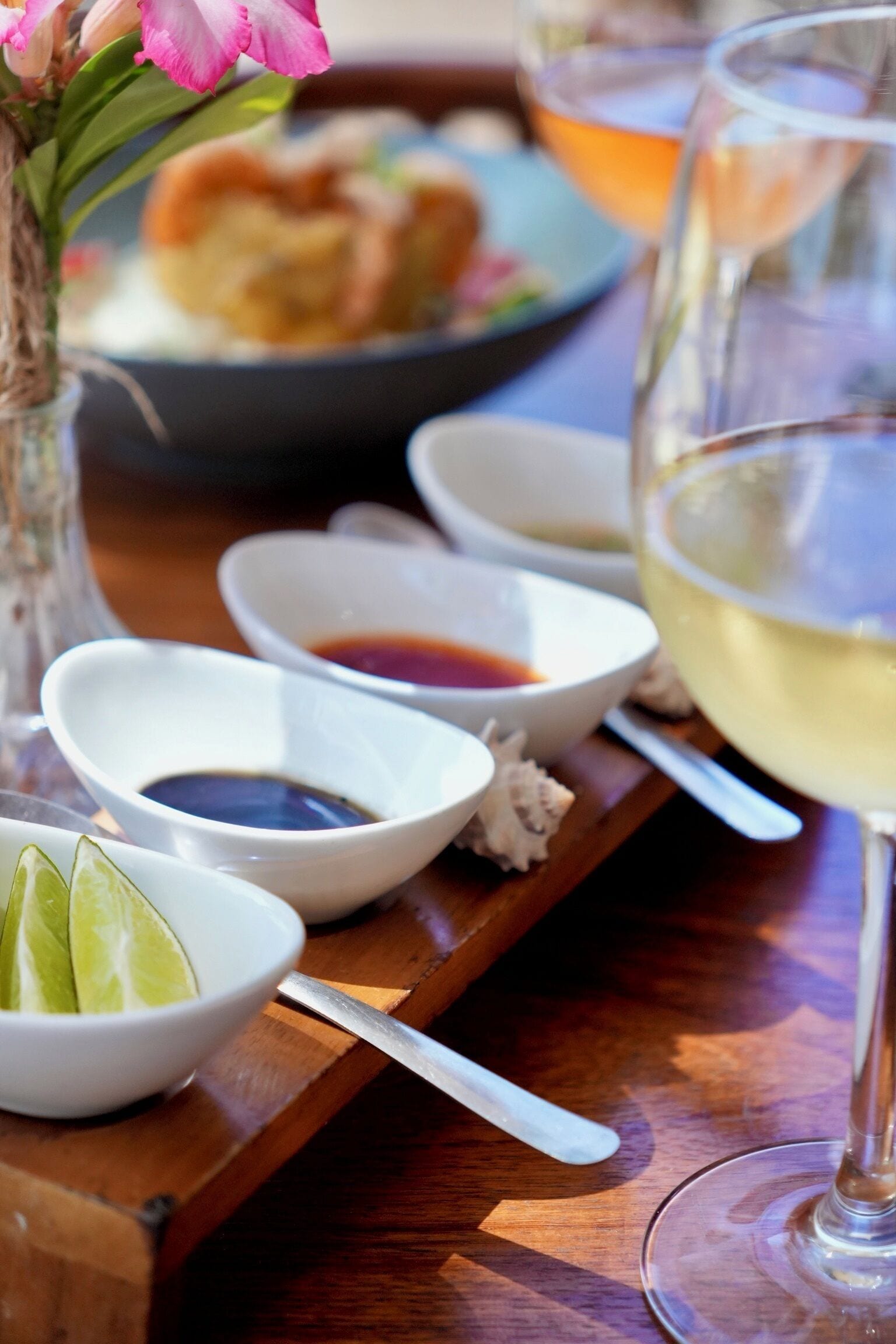 Una bandeja de madera con recipientes de condimentos, una copa de vino blanco y un plato de comida.