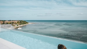 Una persona sentada junto a una piscina con vistas al océano y a una costa distante.