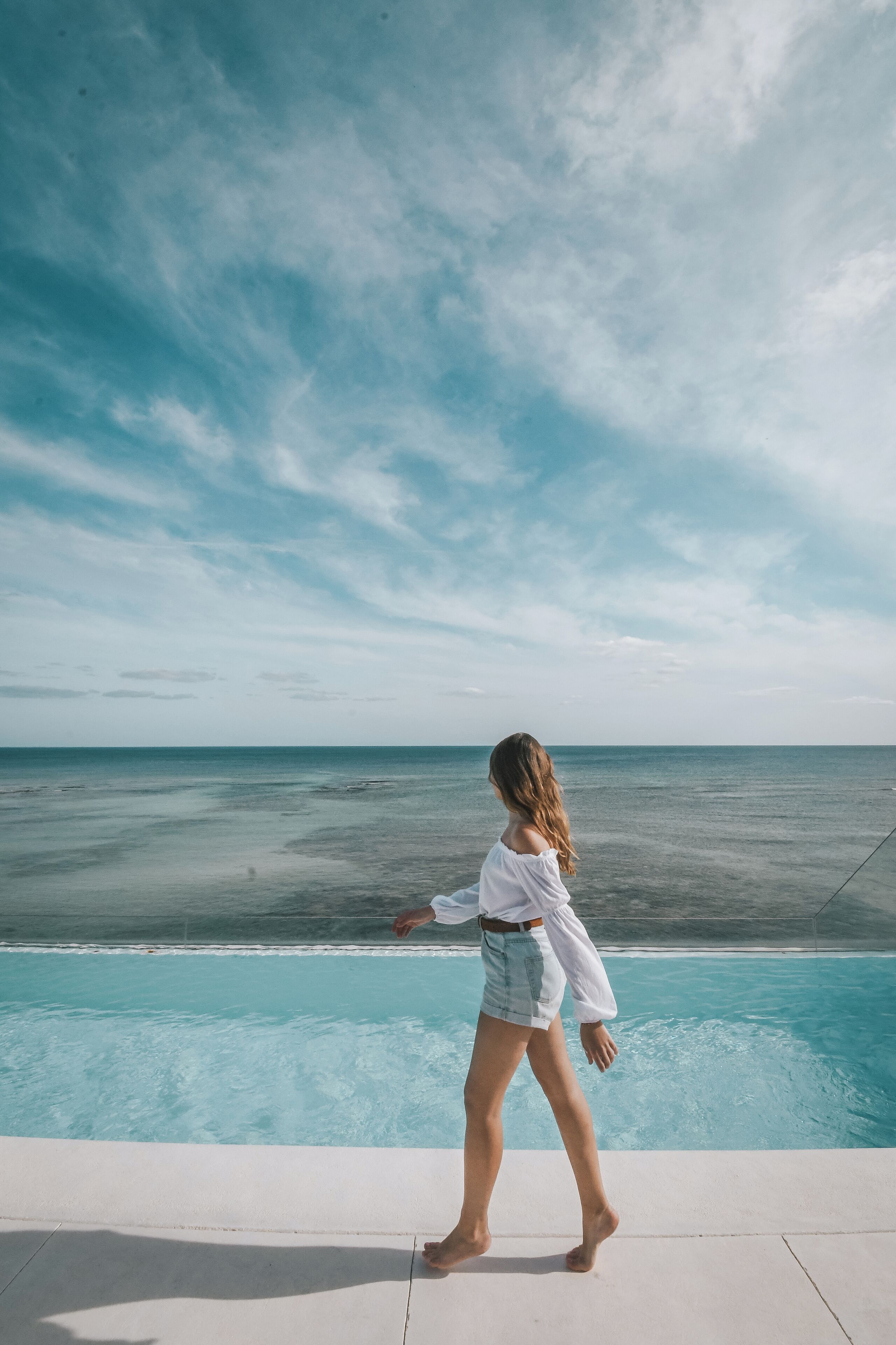 Una persona caminando junto a una piscina con vista al océano.