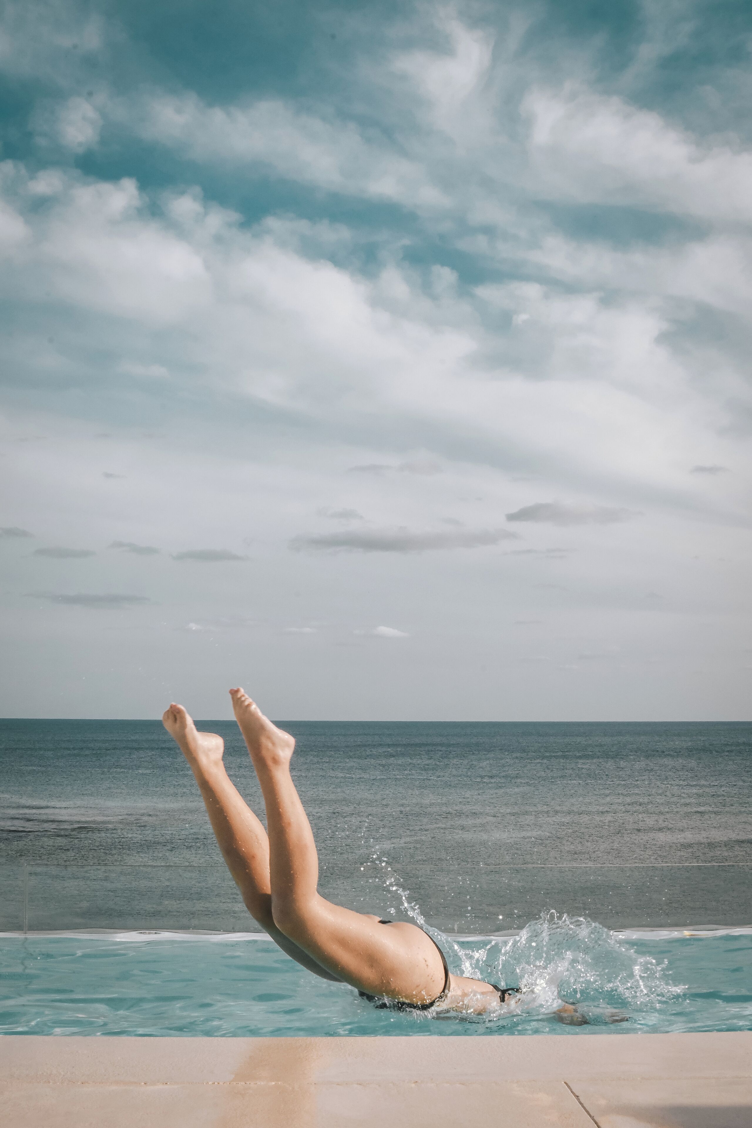 A person diving into a pool with a view of the ocean and sky in the background.