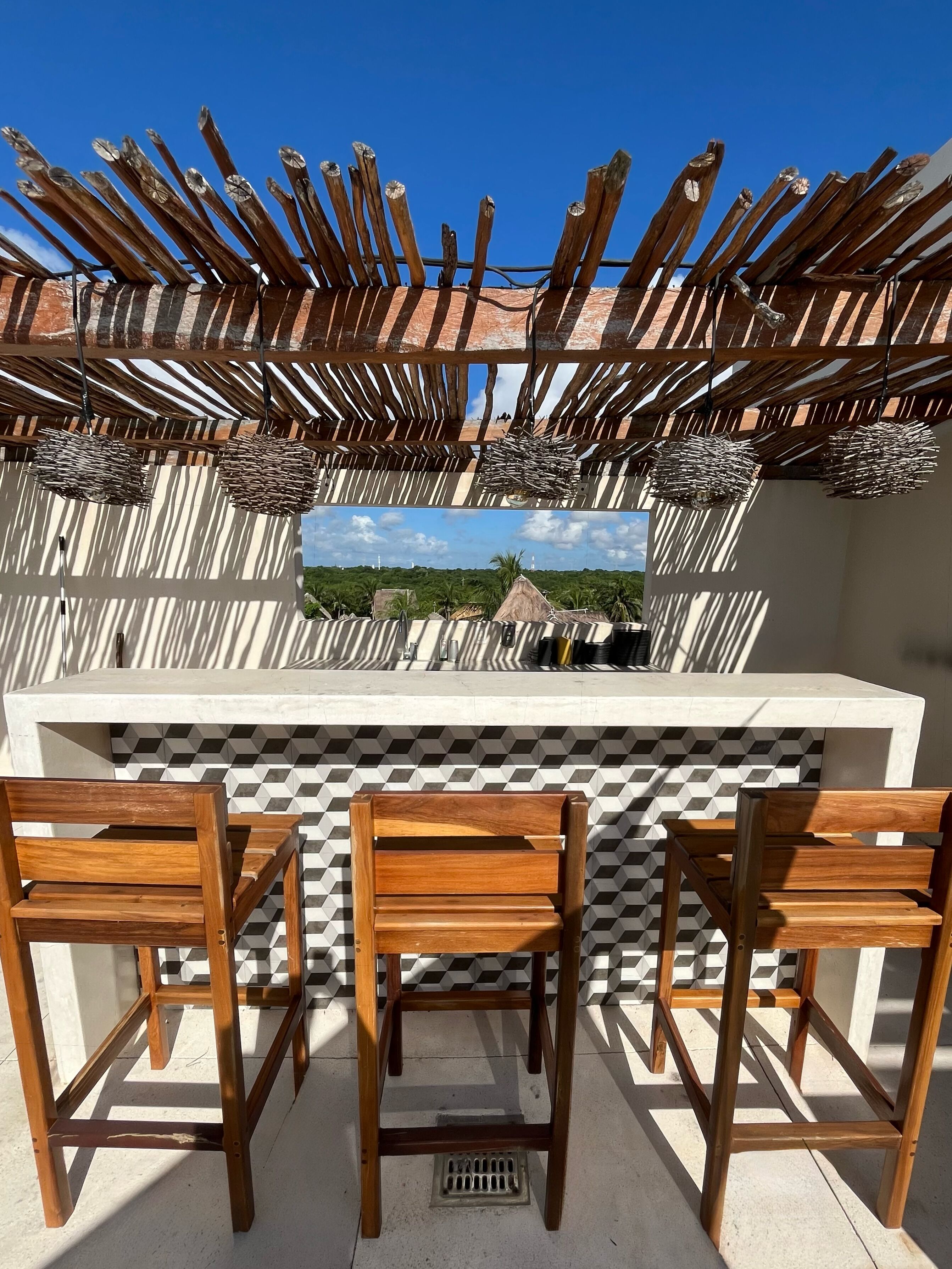 A wooden outdoor seating area with a view of a landscape, a tiled backsplash, and a hanging light fixture.