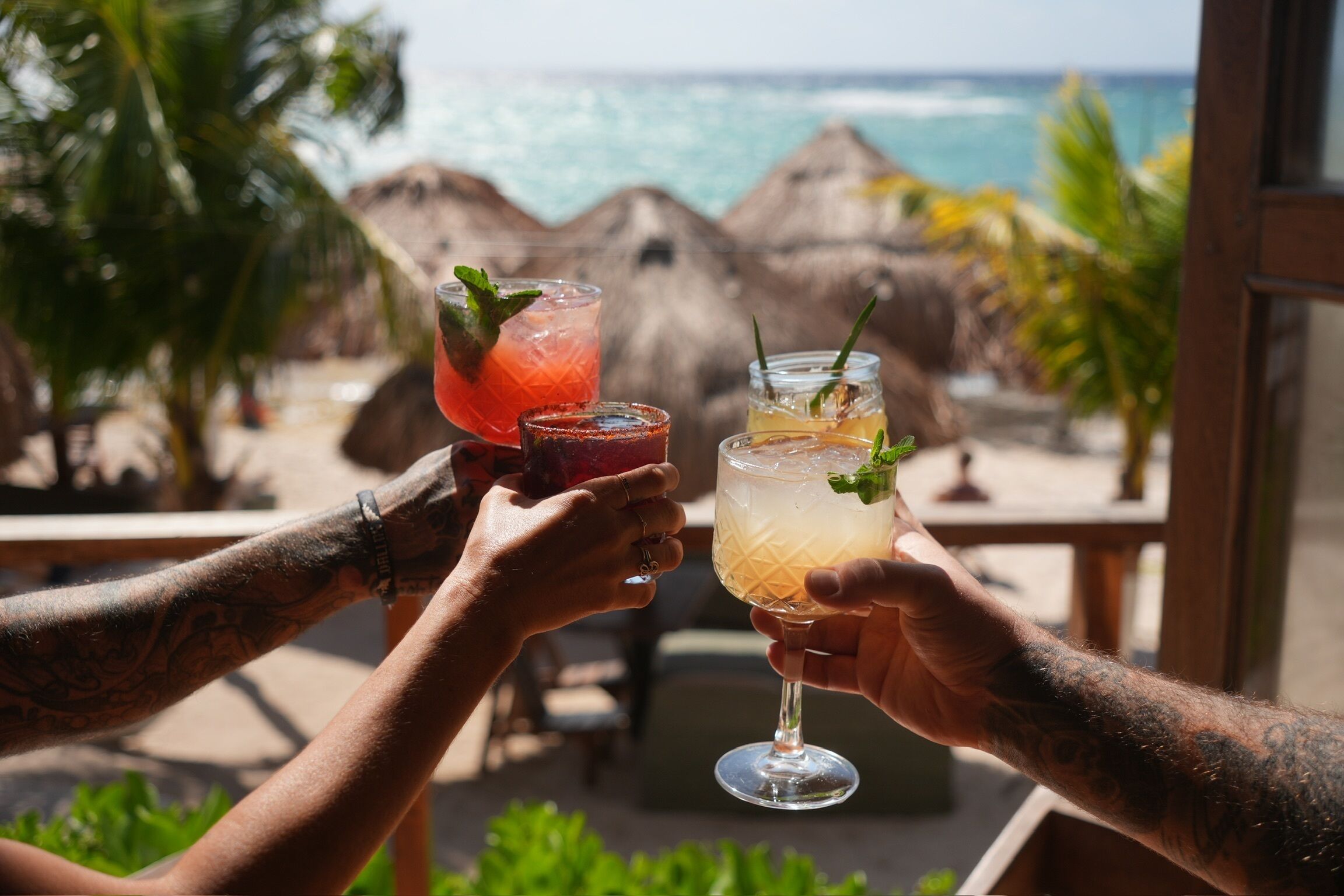 Zwei Personen stoßen an einem Strandbar mit Blick auf das Meer mit Getränken an.