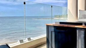 Un balcón moderno con vista al mar, una zona de bar y un área de estar con cojines.