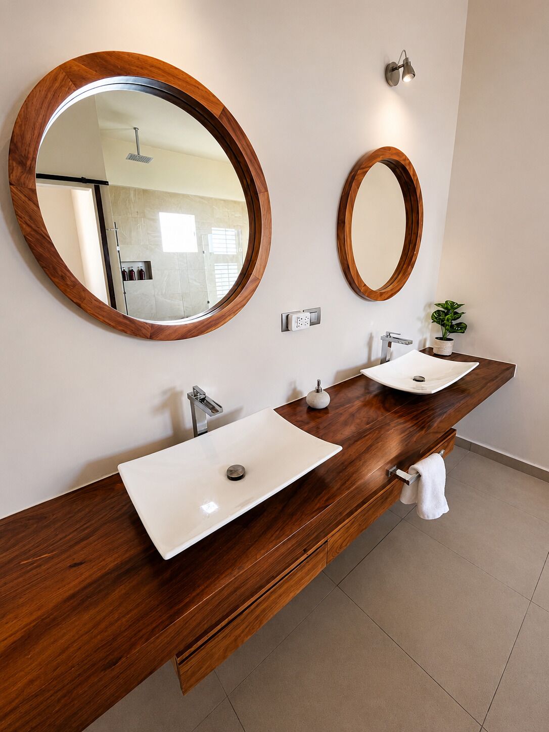 Un baño moderno con dos lavamanos, tocador de madera, espejos grandes y una pequeña planta en maceta.