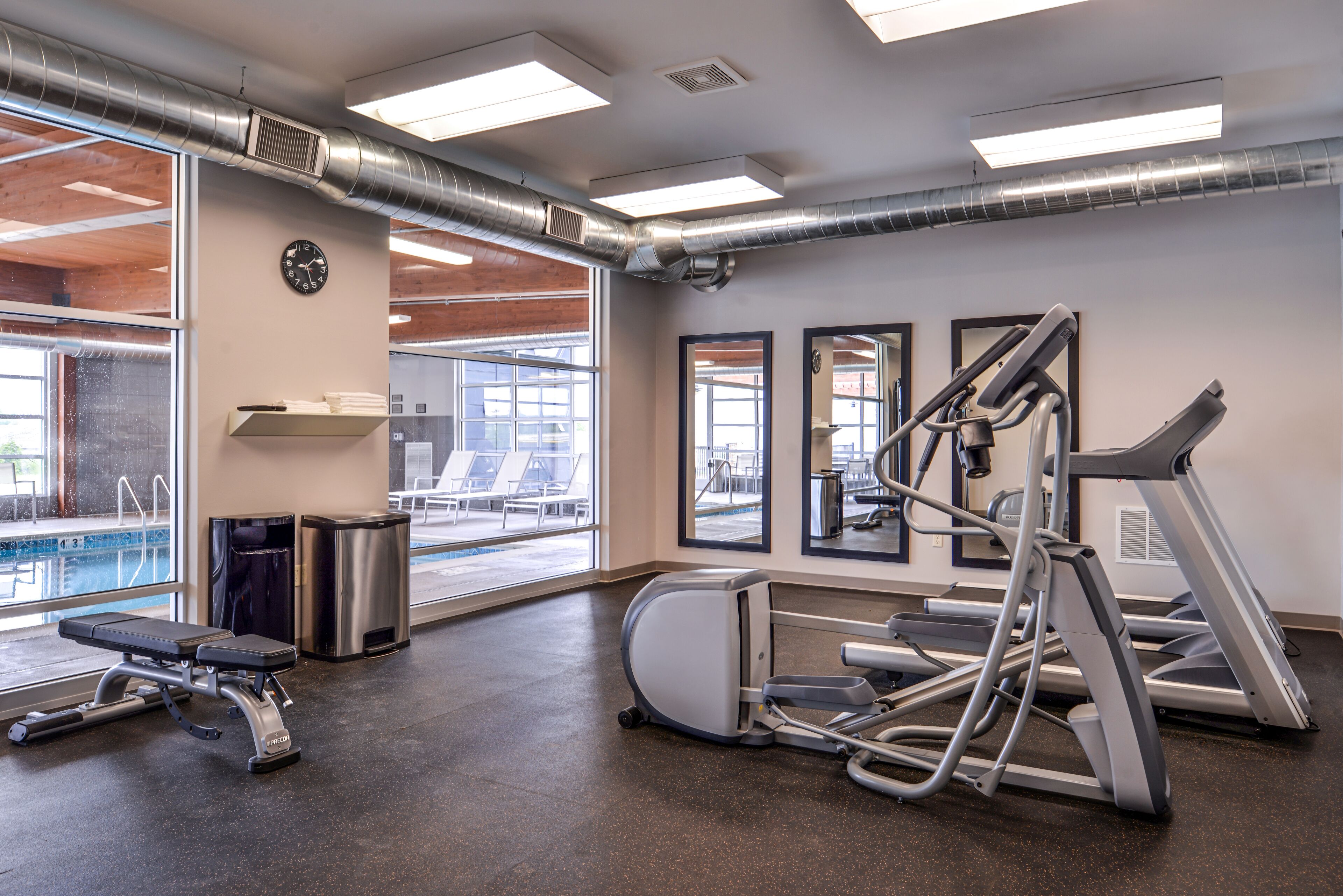A gym with exercise equipment, a clock, and a view of a pool.