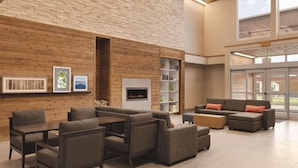 A spacious lobby with a high ceiling, wooden panel walls, a fireplace, and a seating area with sofas and tables. - Country Inn & Suites by Radisson, Ft. Atkinson, WI (Fort Atkinson)