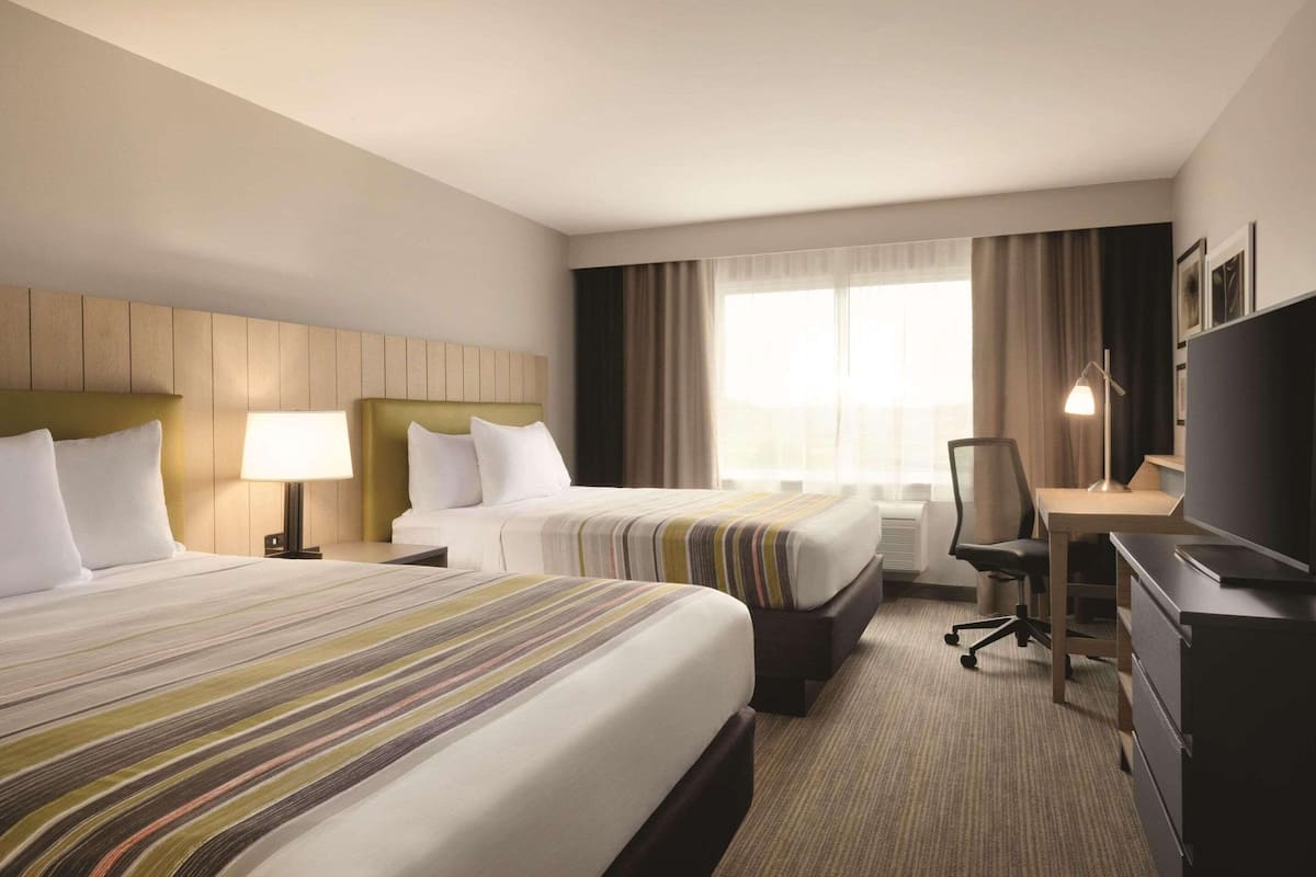 A hotel room with two beds, a desk, a chair, and a TV.