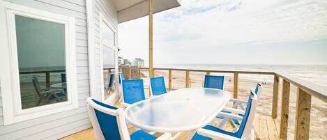 Terraza cubierta al aire libre con una mesa y sillas, con vista a una playa.