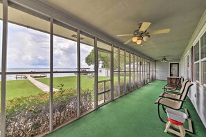 Eine überdachte Veranda mit Blick auf das Meer, grüner Kunstrasen und Gartenmöbel.