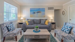 A living room with a grey sofa, two patterned armchairs, a coffee table with a vase, a painting of a boat on the wall, and a clock. - Beautiful Apartment @ The Botanical Gardens #6 (San Antonio)