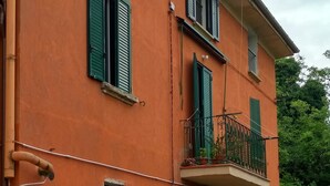 A two-story building with green shutters, a balcony with a metal railing, and potted plants on the ground floor. - Pisolo home holidays near city center and Sant'Orsola Hospital (Bologna)