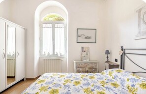 A bedroom with a bed, a wardrobe, a window with curtains, a bedside table, and a wall-mounted picture.