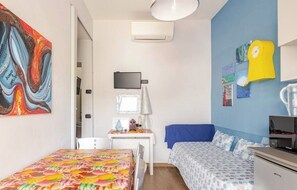 A bedroom with a bed, a desk with a lamp, a TV, and artwork on the walls.