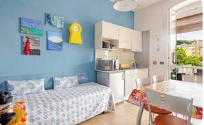A bedroom with a bed, a small kitchenette, a dining table, and a view of buildings.