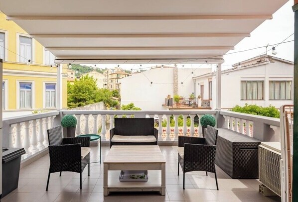 A balcony with outdoor furniture, a white awning, and a view of neighboring buildings.