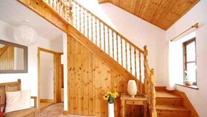 Un escalier en bois menant à l’étage supérieur, un banc en bois, un vase rempli de fleurs et une fenêtre offrant une vue agréable.