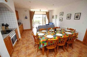 A dining area with a tiled floor, wooden chairs, a table with a colorful tablecloth, and a view through a window.