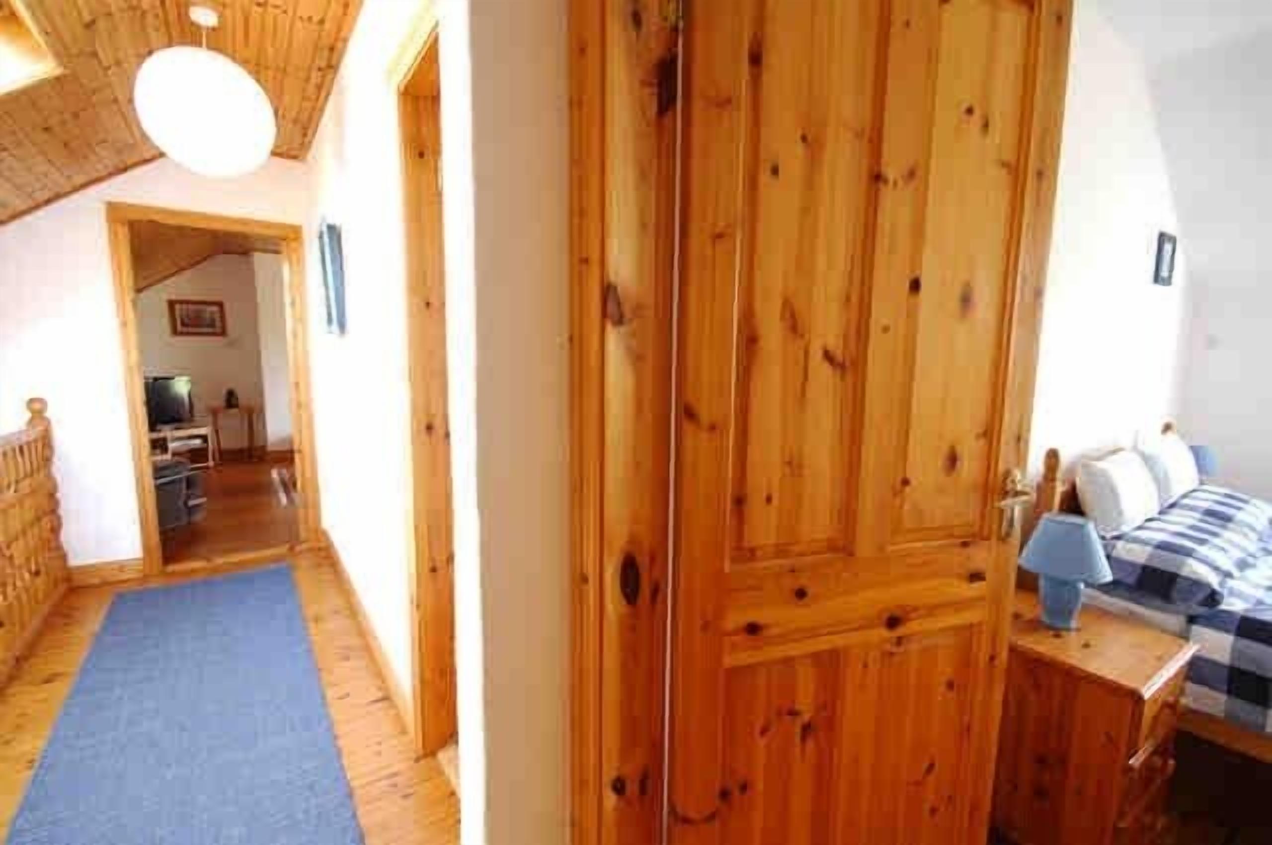 A wooden door leading to a bedroom with a checkered bedspread and a nightstand.