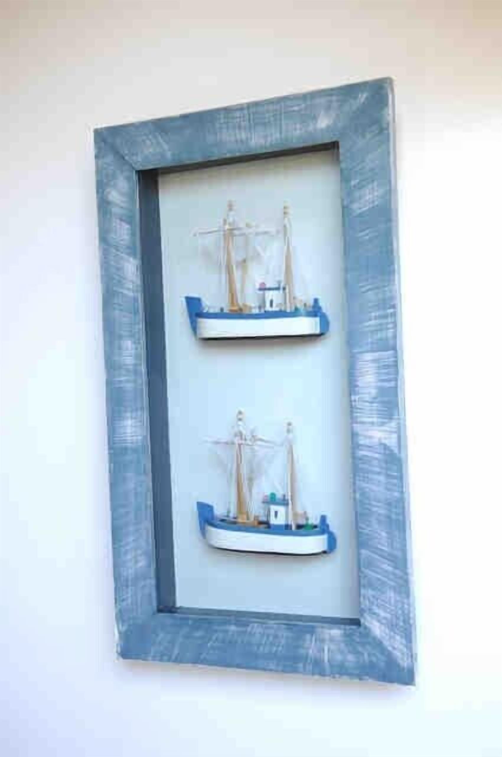 A framed nautical model with two ships, one larger and one smaller, on a white wall.