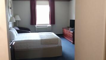 A hotel room with a bed, a desk, a chair, a dresser, a lamp, and a window with curtains.