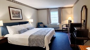 A hotel room with a bed, bedside lamps, a desk, a chair, a TV, and a window with curtains. - Dawson Inn (Meadow Bridge)