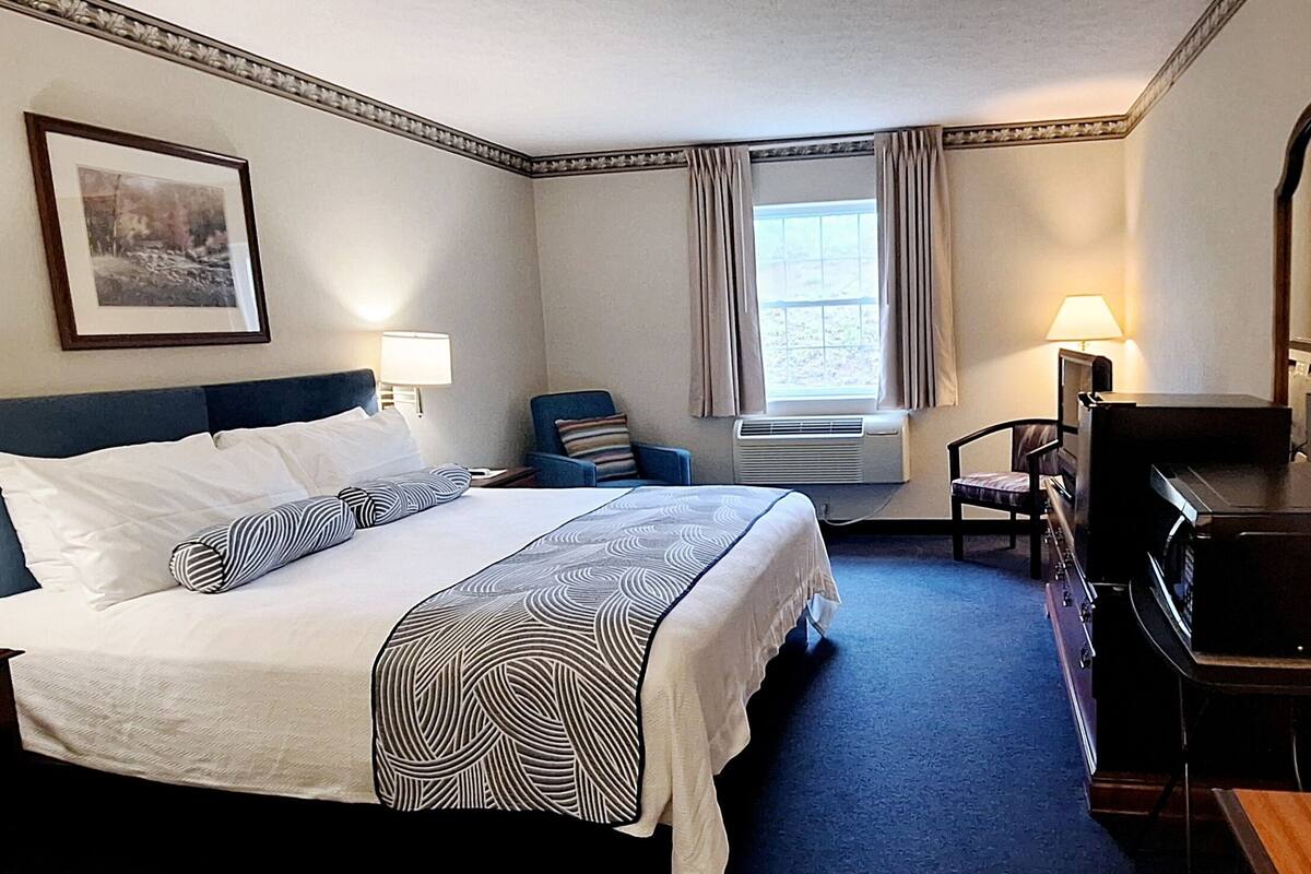 A hotel room with a bed, bedside lamps, a desk, a chair, a TV, and a window with curtains.