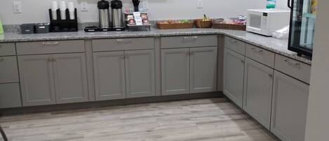 A modern kitchen with grey cabinets, a granite countertop, and a large landscape painting above the sink.