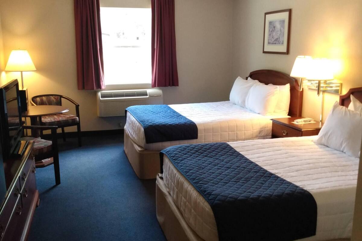 A hotel room with two beds, a desk, a chair, and a window with curtains.