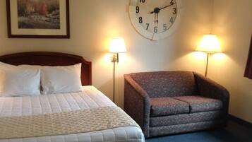 A hotel room with a bed, a chair, two wall lamps, and a clock.