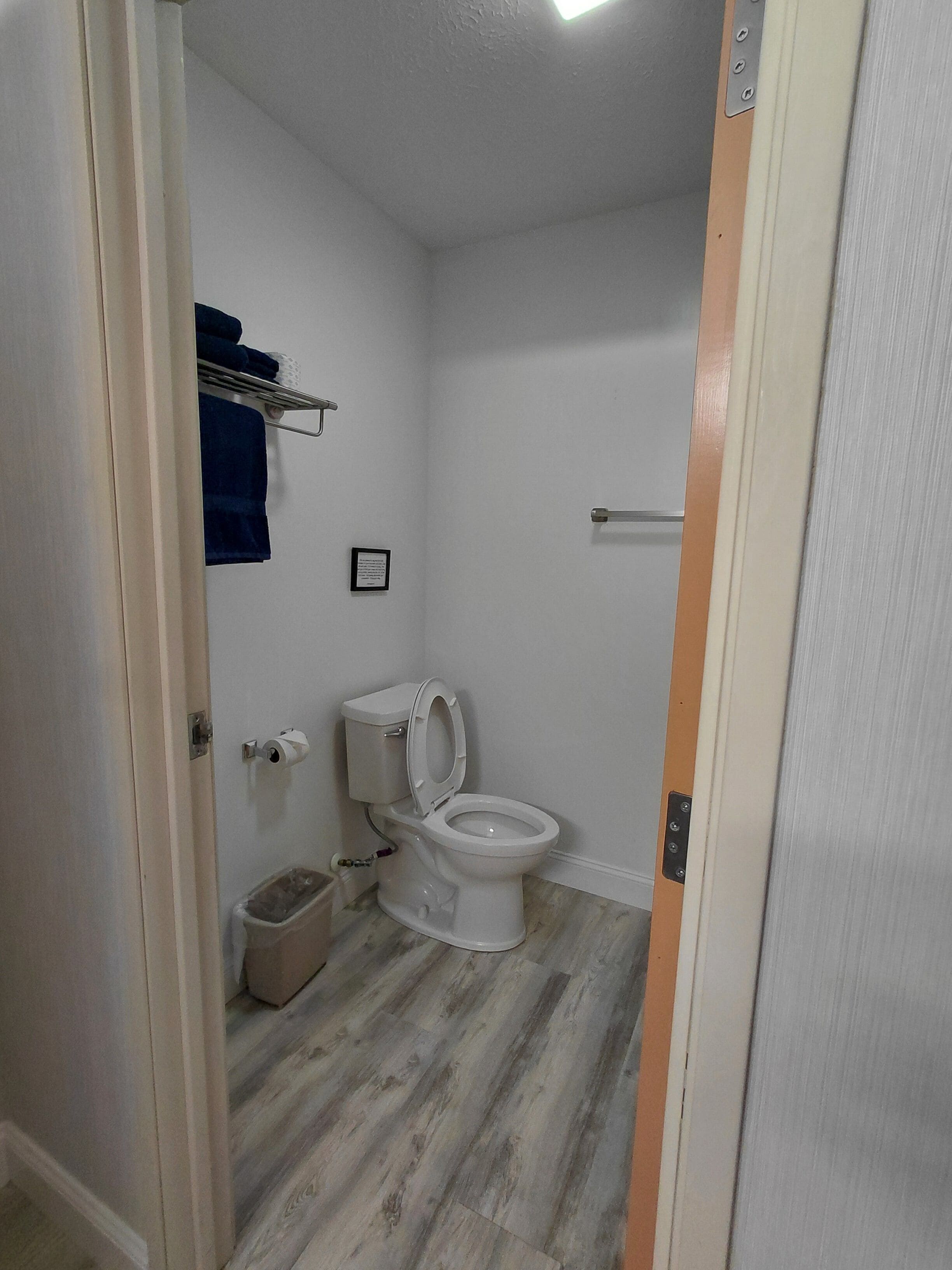 Un baño con inodoro, un cubo de basura y un perchero con una toalla azul.
