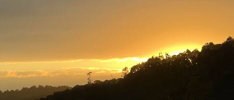 A sunset over a hilly landscape with a road and a bridge in the foreground.