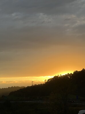 A sunset over a hilly landscape with a road and a bridge in the foreground.