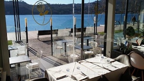 An outdoor dining area with tables and chairs, overlooking a body of water and hills. - Duomo Hotel (Toscolano Maderno)