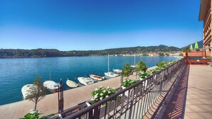 A waterfront balcony with a view of the sea, boats docked, and a cityscape in the background. - Duomo Hotel (Toscolano Maderno)