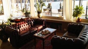 Ein gemütliches Wohnzimmer mit Ledersofa, Couchtisch und Blick auf einen See und eine Statue.