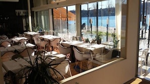 An indoor dining area with tables and chairs, large windows with a view of a lake and outdoor seating. - Duomo Hotel (Toscolano Maderno)