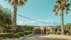A paved driveway leading to a gated entrance with a brick wall and a metal gate. - Villa 'Oasis' with exclusive pool (Siracusa)