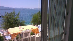 A balcony with a table and chairs, overlooking a body of water and distant mountains. - Romantic, quite, seafront apartment, sunbeds, barbecue, all by the sea. For 2p (Komarna)