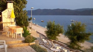 A terrace with outdoor seating, a table, and chairs overlooking a lake with boats. - Romantic, quite, seafront apartment, sunbeds, barbecue, all by the sea. For 2p (Komarna)