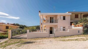 A two-story residential building with a balcony, a gated entrance, and a clear sky. - Villa with terrace and washing machine (Cala Gonone)