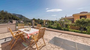 A patio with a table and chairs, a metal gate, and a mountain in the background. - Villa with terrace and washing machine (Cala Gonone)