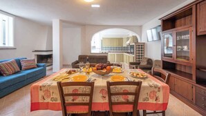 A dining area with a table set for four, a blue sofa, and a kitchen in the background. - Villa with terrace and washing machine (Cala Gonone)