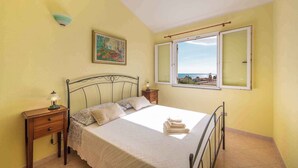 A bedroom with a bed, bedside tables, a lamp, a painting, and a window with a view. - Villa with terrace and washing machine (Cala Gonone)