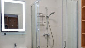 Un baño con ducha acristalada, lavamanos, espejo y lavadora.